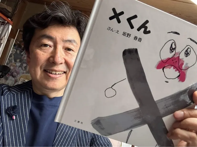 絵本「X(バツ)くん」を手に微笑むお父様の坂野貴宏さん